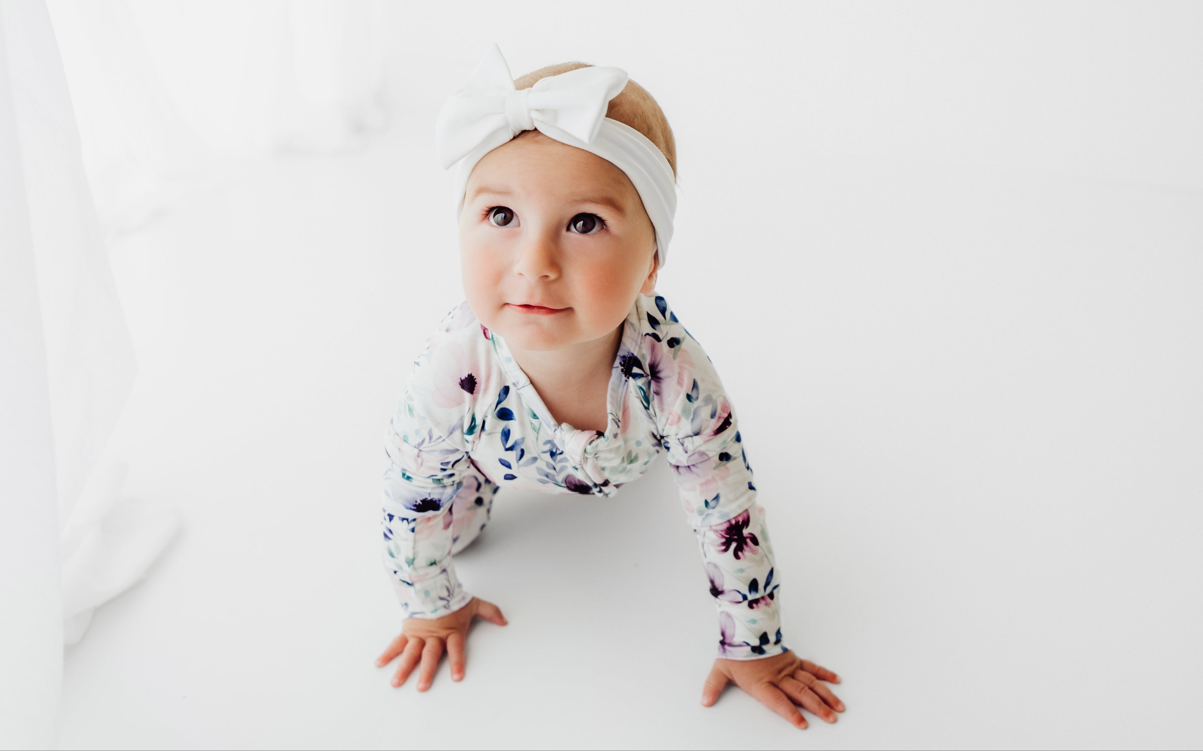 Baby wearing a floral onesie and headband on a white background